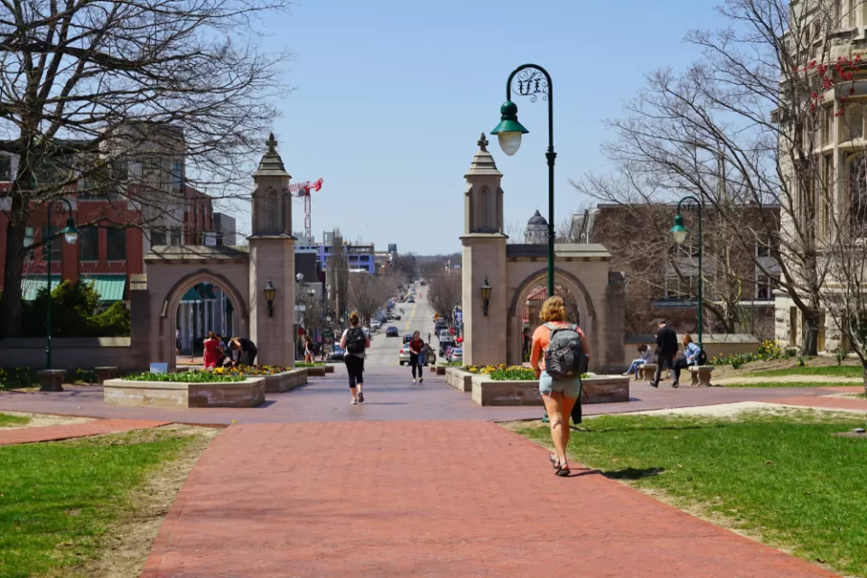 An image of the Sample Gates at the entrance of the college campus of Indiana University Bloomington, with a street and the city in the background.